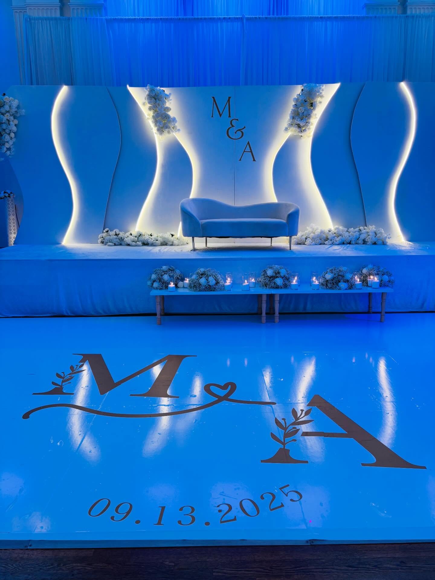 Blue and white wedding stage with illuminated backdrop, flowers, and custom initials